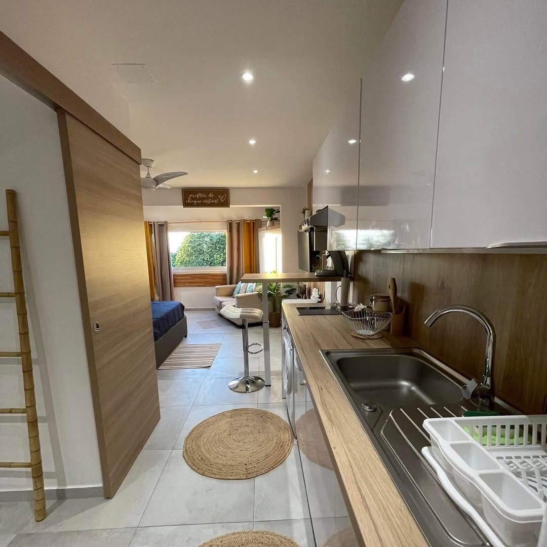 Le studio Hei : cuisine équipée en bois clair, coin salon et baie vitrée sur la verdure